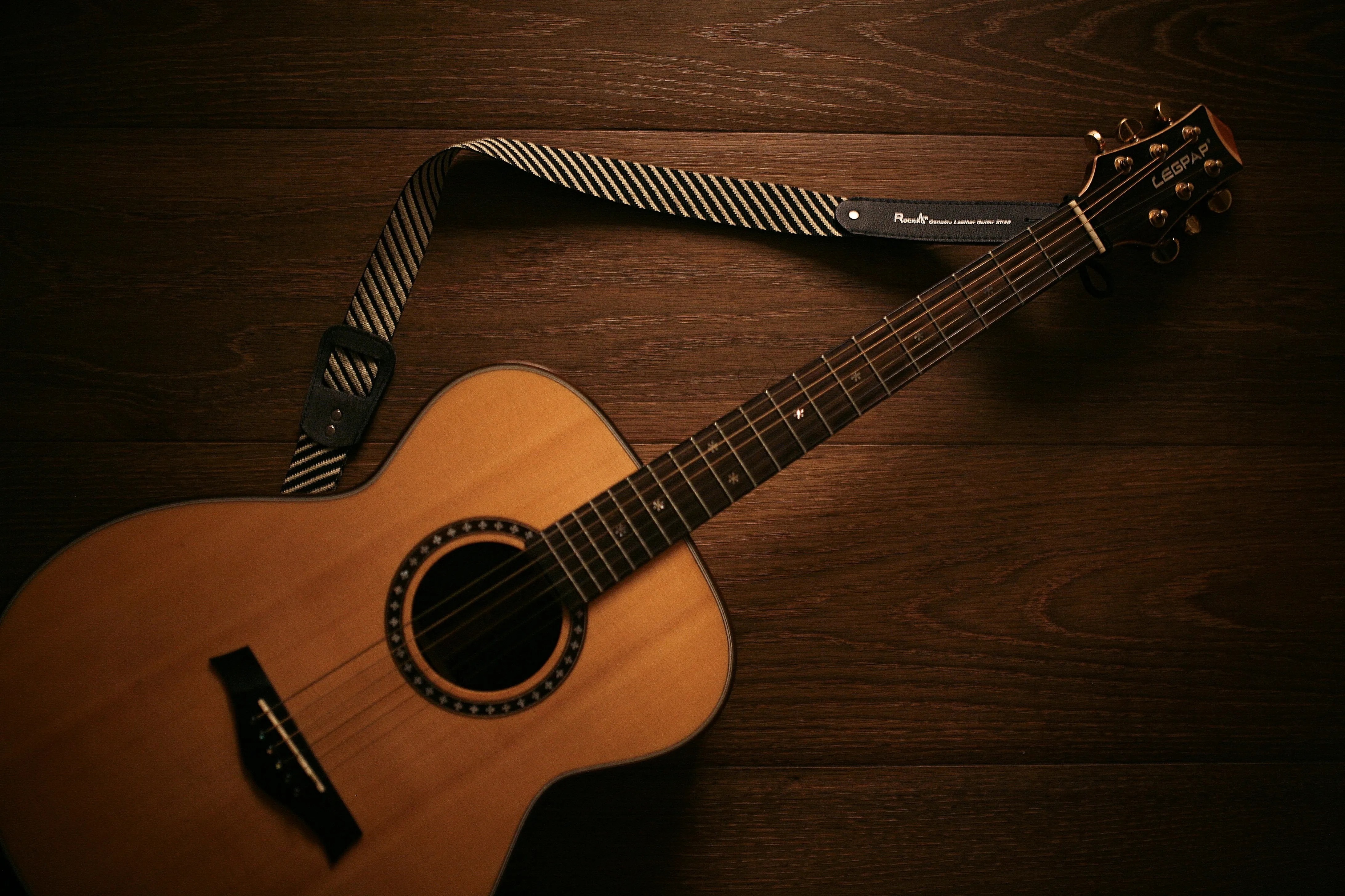 Acoustic guitar with strap laid on a wooden floor — a reminder that the right setup starts before you ever play a note