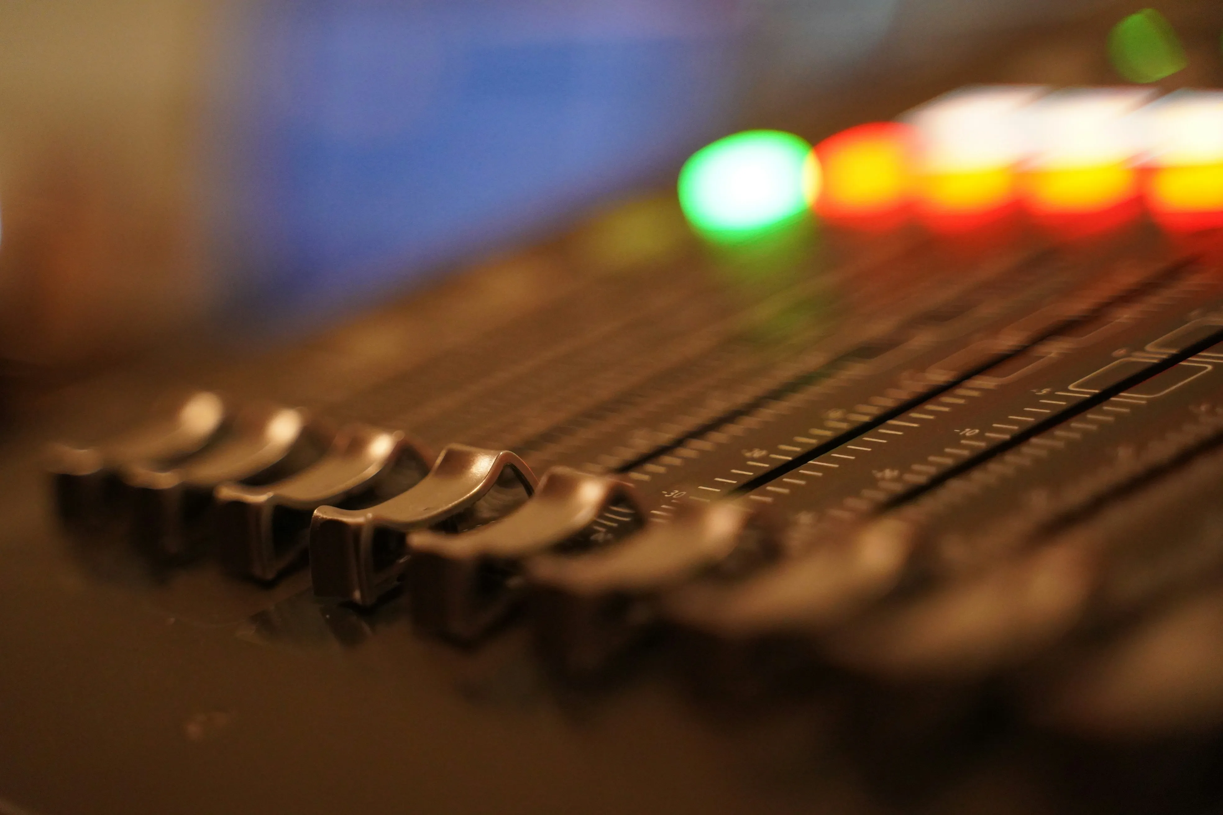 Close-up of a mixing board's fader bank with green and red LED level meters glowing — the kind of moment every church sound tech lives for