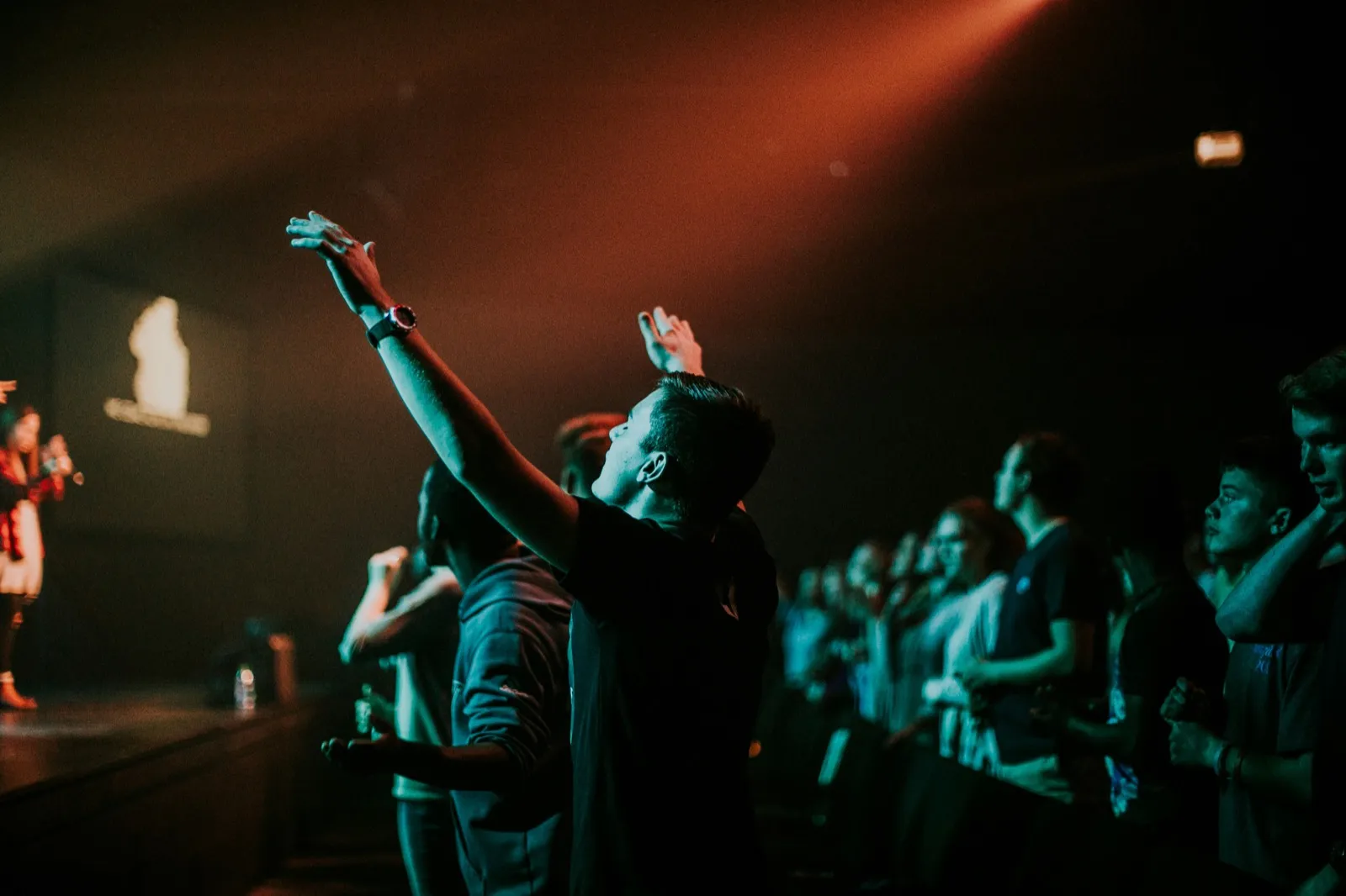 Worshiper with hands raised toward the stage in a darkened church