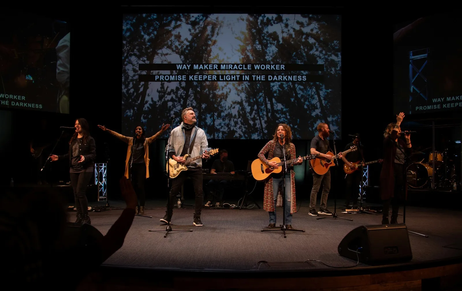 Worship team leading congregation singing Way Maker on a lit stage